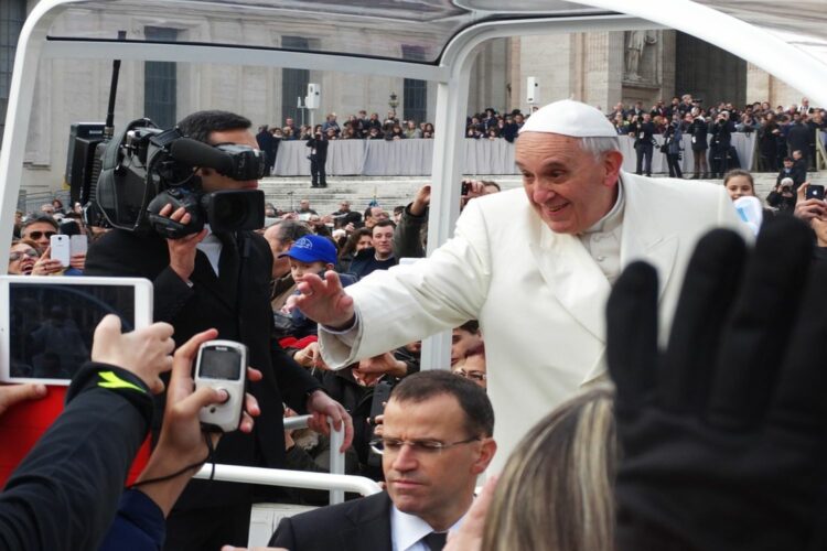 El Papa Francisco con sotana blanca en vehículo, rodeado de muchedumbre que le hace fotos con teléfonos móviles.