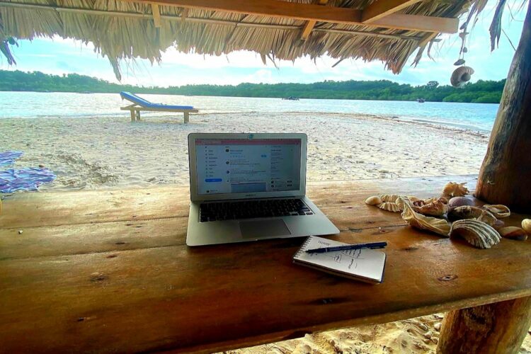 Ordenador portátil en mesa de madera con playa de fondo.