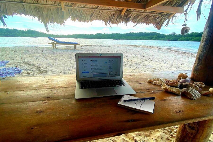 Ordenador portátil en mesa de madera con playa de fondo.