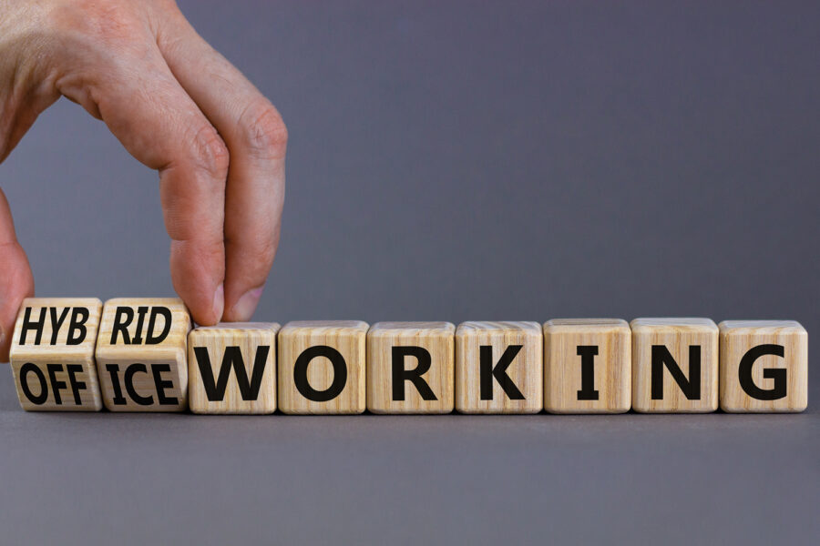 Hybrid or office working symbol. Businessman turns cubes and changes words 'office working' to 'hybrid working'. Beautiful grey background. Business, hybrid or office working concept, copy space.